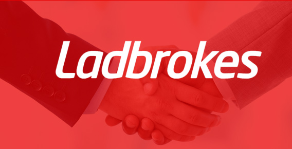 Two men in suits shaking hands behind Ladbrokes logo
